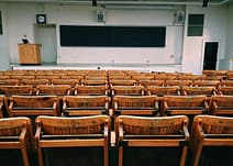 gallery-2 An empty lecture hall featuring wooden chairs and a large blackboard.