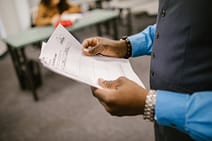 gallery-4 An instructor examining test papers in a classroom setting, focusing on education and evaluation.
