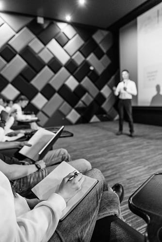 gallery-6 Black and white shot of students taking notes during a lecture in a modern hall.