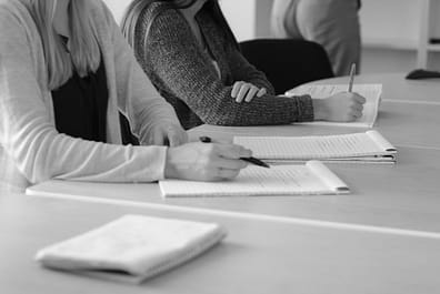 about-img Black and white image of students writing notes during a meeting.