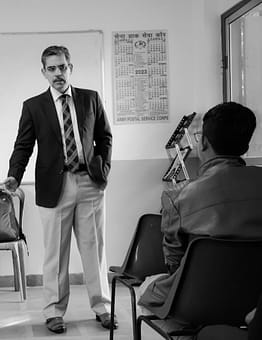 services-01 Adult man in a black blazer giving a presentation to attendees in a classroom setting.