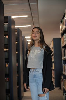 services-03 A young woman stands amidst library shelves, capturing the essence of learning.