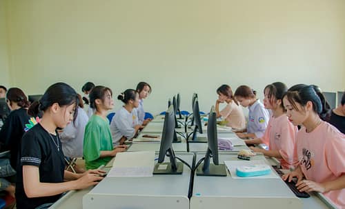 why-choose-us Group of female students studying at computers in a classroom setting.